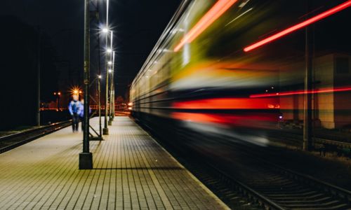 Frecciarossa sfreccia in una stazione notturna con scie luminose rosse e passeggeri sul marciapiede