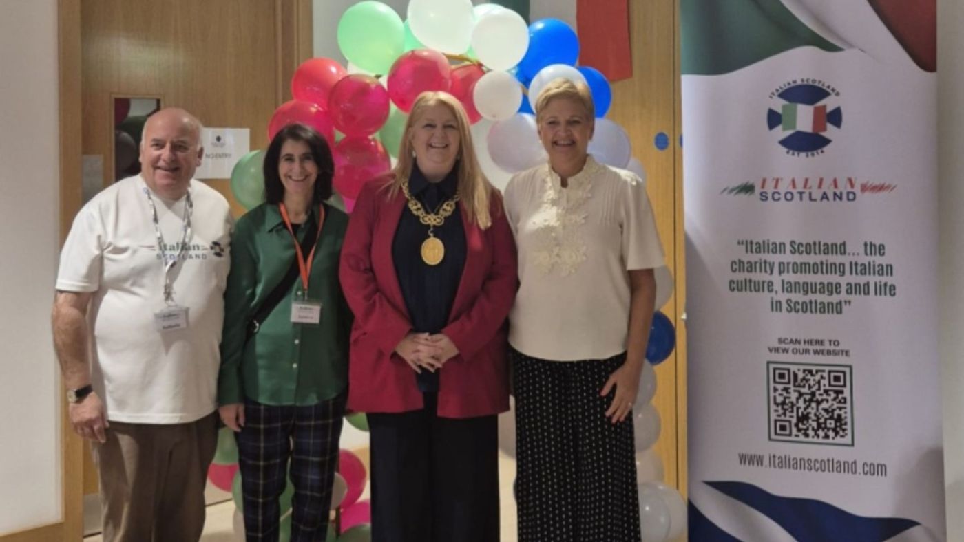 Quattro persone posano sorridenti di fronte a palloncini colorati e al banner dell’associazione Italian Scotland durante la Festa Italiana.