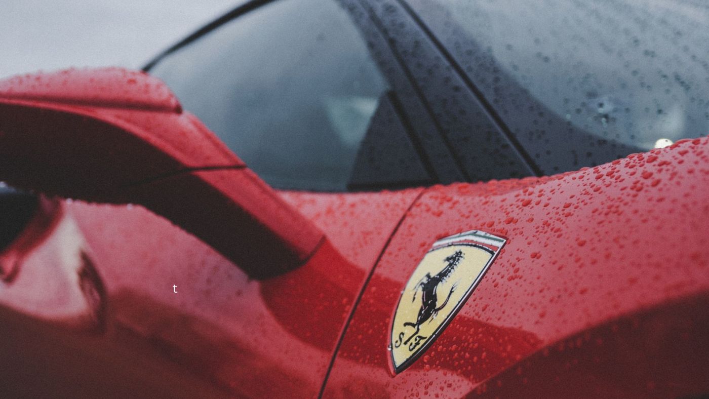 Particolare di una Ferrari rossa sotto la pioggia con il logo del Cavallino Rampante in primo piano