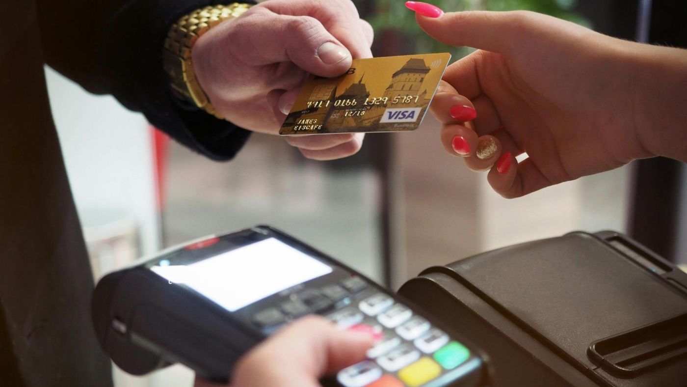 Primo piano di mani che scambiano una carta di credito oro sopra un terminale di pagamento, simbolo di transazioni ad alto valore