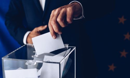 Primo piano di una mano che inserisce una scheda elettorale in un'urna, simbolo delle elezioni regionali in Calabria 2025