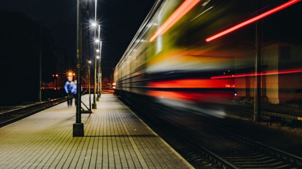 Frecciarossa sfreccia in una stazione notturna con scie luminose rosse e passeggeri sul marciapiede