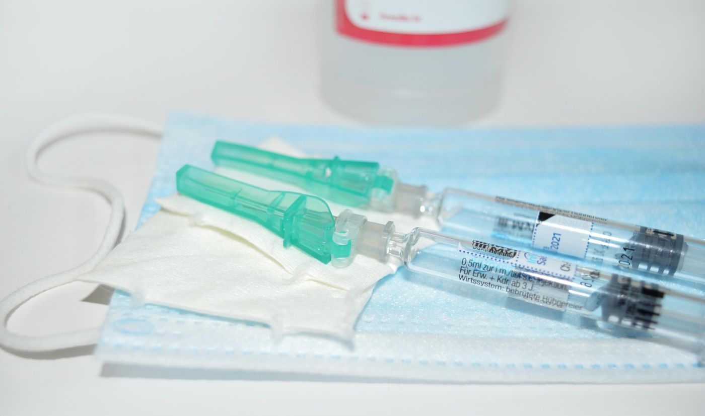 Due siringhe monouso con cappucci verdi poggiano su una mascherina chirurgica e una garza, simbolo di vaccinazione