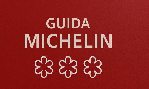 Copertina della Guida Michelin con sfondo rosso e tre stelle, simbolo della valutazione culinaria.