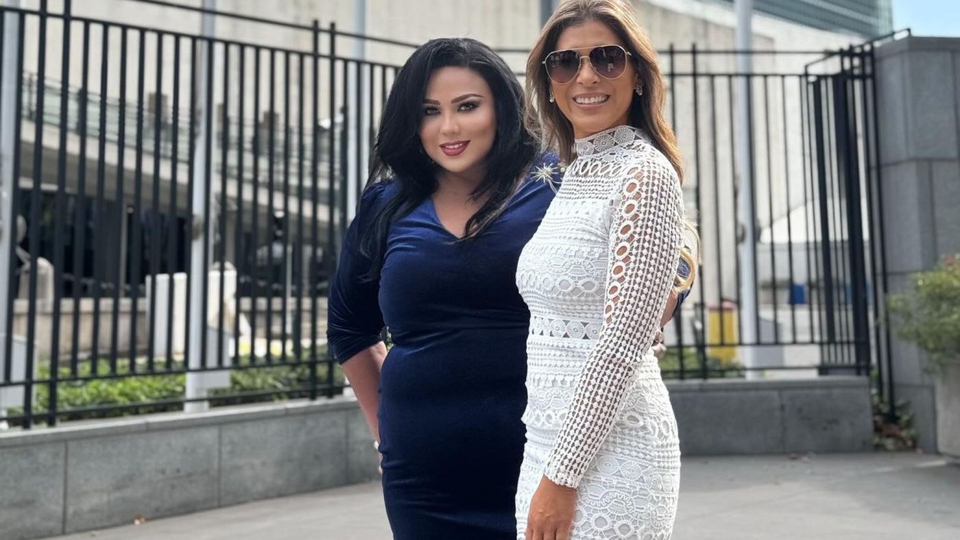 Due donne sorridenti davanti alla sede dell'ONU, in abiti eleganti, partecipano a un evento internazionale.