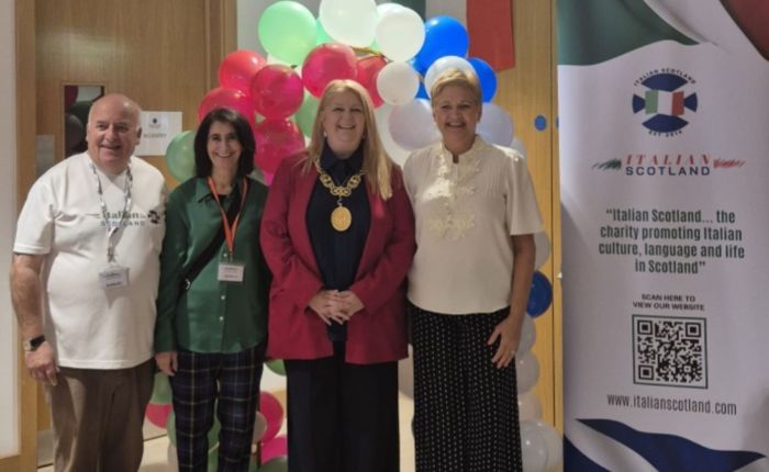 Quattro persone posano sorridenti di fronte a palloncini colorati e al banner dell’associazione Italian Scotland durante la Festa Italiana.