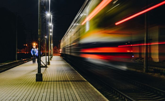 Frecciarossa sfreccia in una stazione notturna con scie luminose rosse e passeggeri sul marciapiede