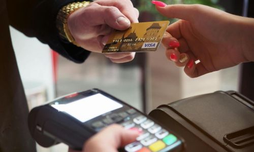 Primo piano di mani che scambiano una carta di credito oro sopra un terminale di pagamento, simbolo di transazioni ad alto valore